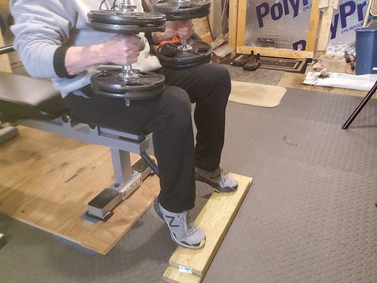 Performing calf raises with dumbbells on lap