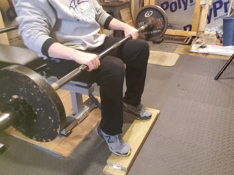Performing calf raises with barbell on lap